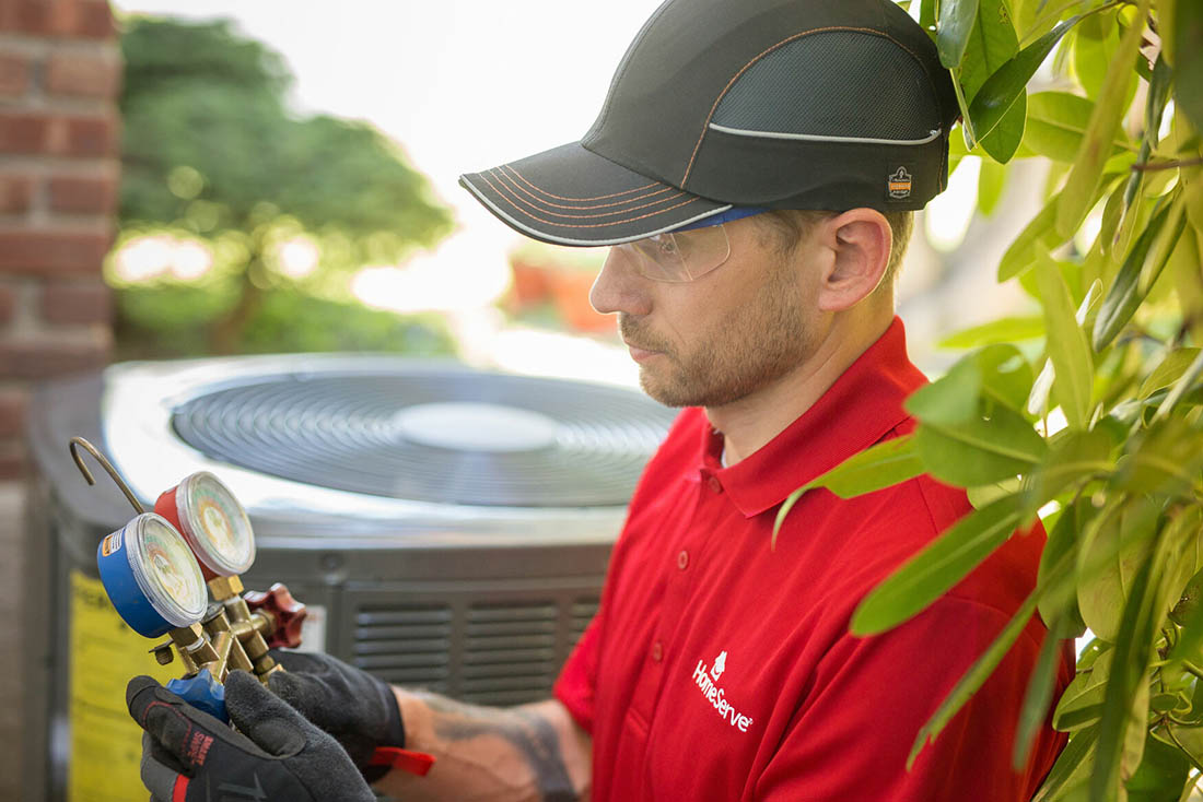 heatPumps-HeatPumpInstallation-Supporting-1100×734 Close-up of man inspecting a tool near a heat pump unit